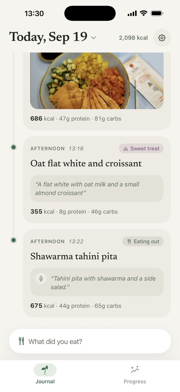 Two saved meals: a typed note, “A flat white with oat milk and a small almond croissant”, at 355 calories, and a spoken one, “Tahini pita with shawarma and a side salad”, at 675 calories.